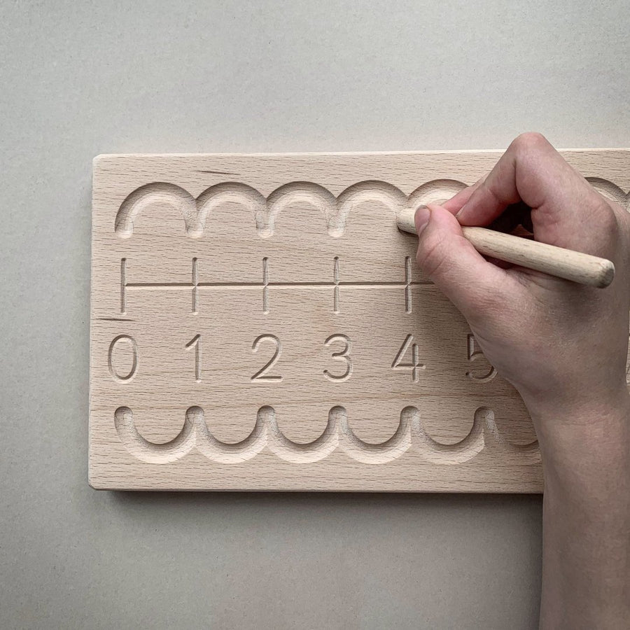 Close up of hand tracing over a Coach House sustainable wooden number line toy on a grey background