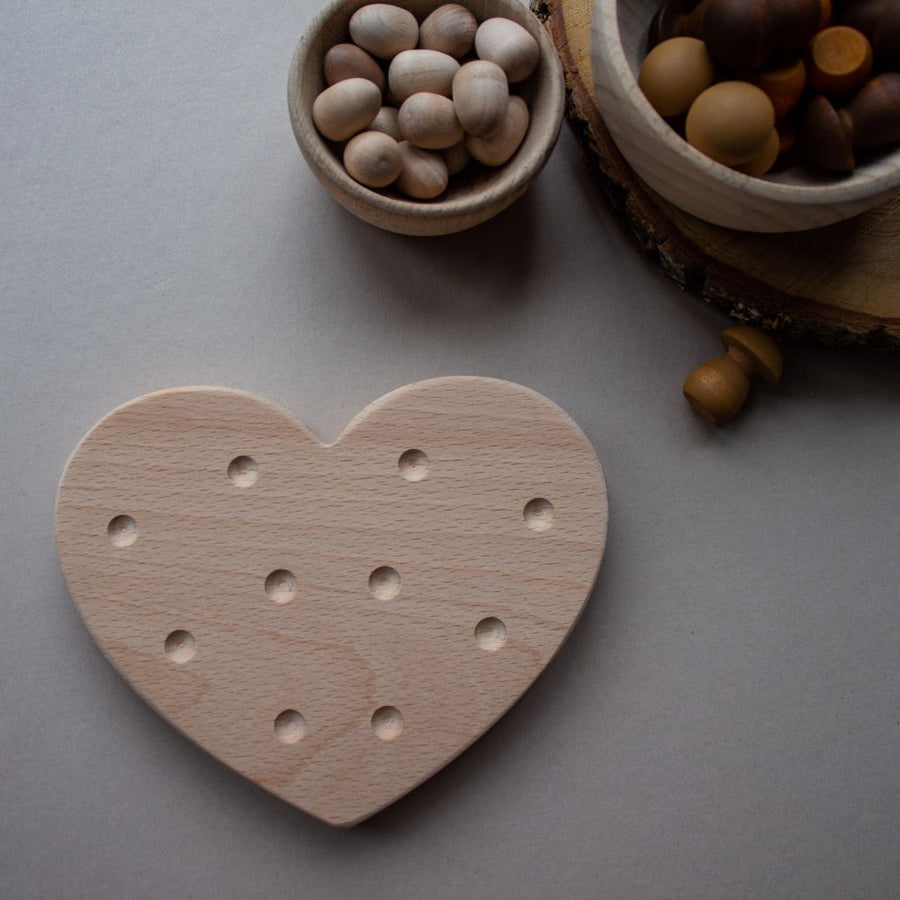 The Coach House Heart Fine Motor Board and a selection of wooden loose parts in bowls. A heart shaped wooden beechwood board with indents to place beads