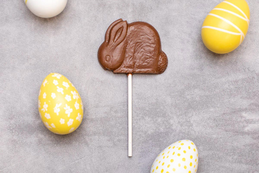 Cocoa Loco eco-friendly 26g chocolate bunny lolly on a grey background next to some yellow and white easter eggs