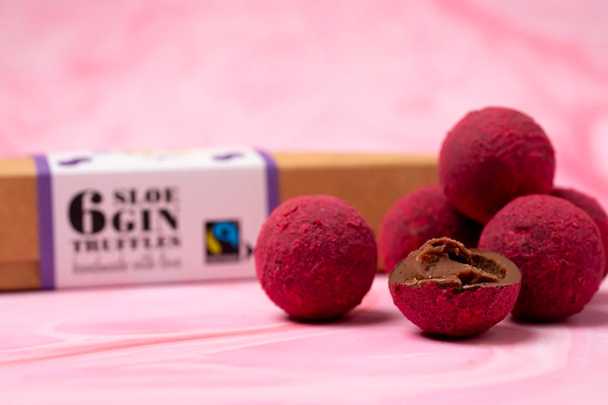 Close up of a pile of Cocoa Loco fairtrade milk chocolate gin truffles on a pink background next to their cardboard box