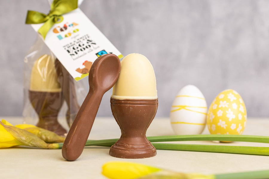 Cocoa Loco eco-friendly fairtrade white and milk chocolate egg and spoon on a cream worktop next to some yellow easter eggs and a daffodil