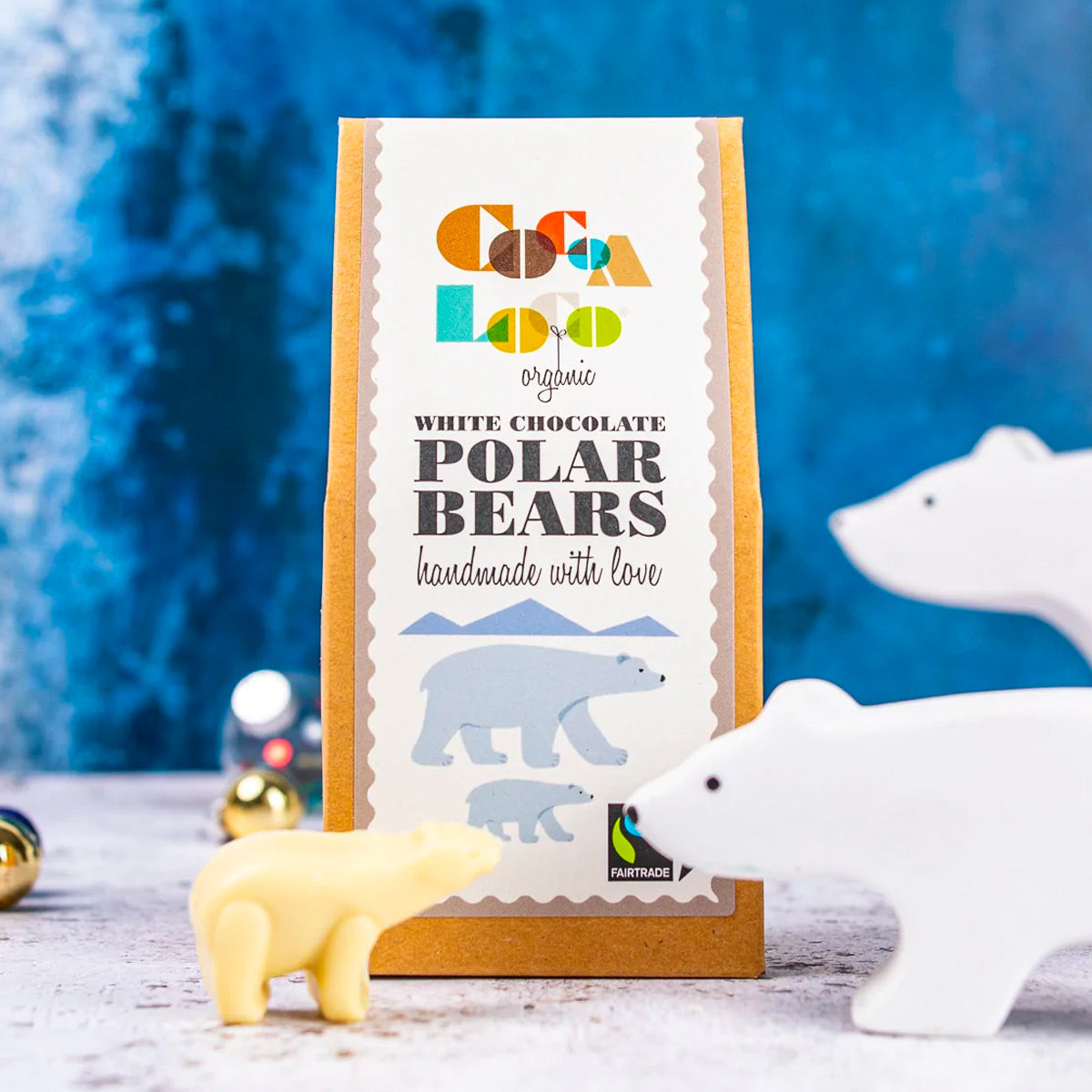 Cocoa Loco organic fairtrade white chocolate polar bears on a blue background next to some wooden toy polar bears