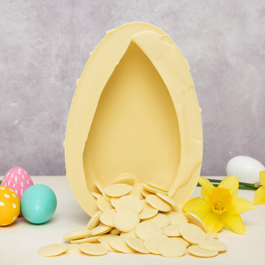 The inside of the Cocoa Loco White Chocolate Lemon Drizzle Easter Egg on a cream table. The egg is open with white chocolate buttons cascading from the inside out