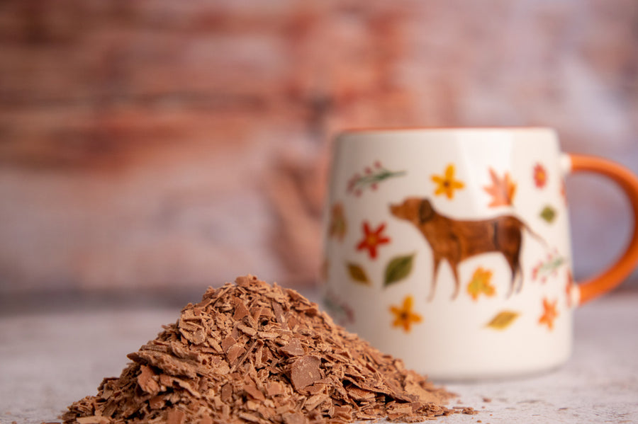 Close up of some Cocoa Loco fairtrade hot chocolate drinking flakes in a pile in front of a white and orange mug