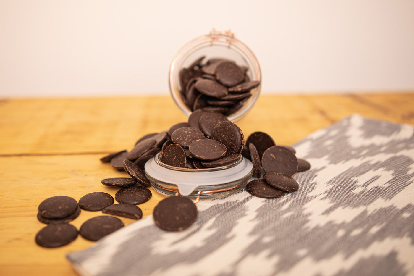 Overturned glass jar of Cocoa Loco vegan dark chocolate buttons on a wooden table