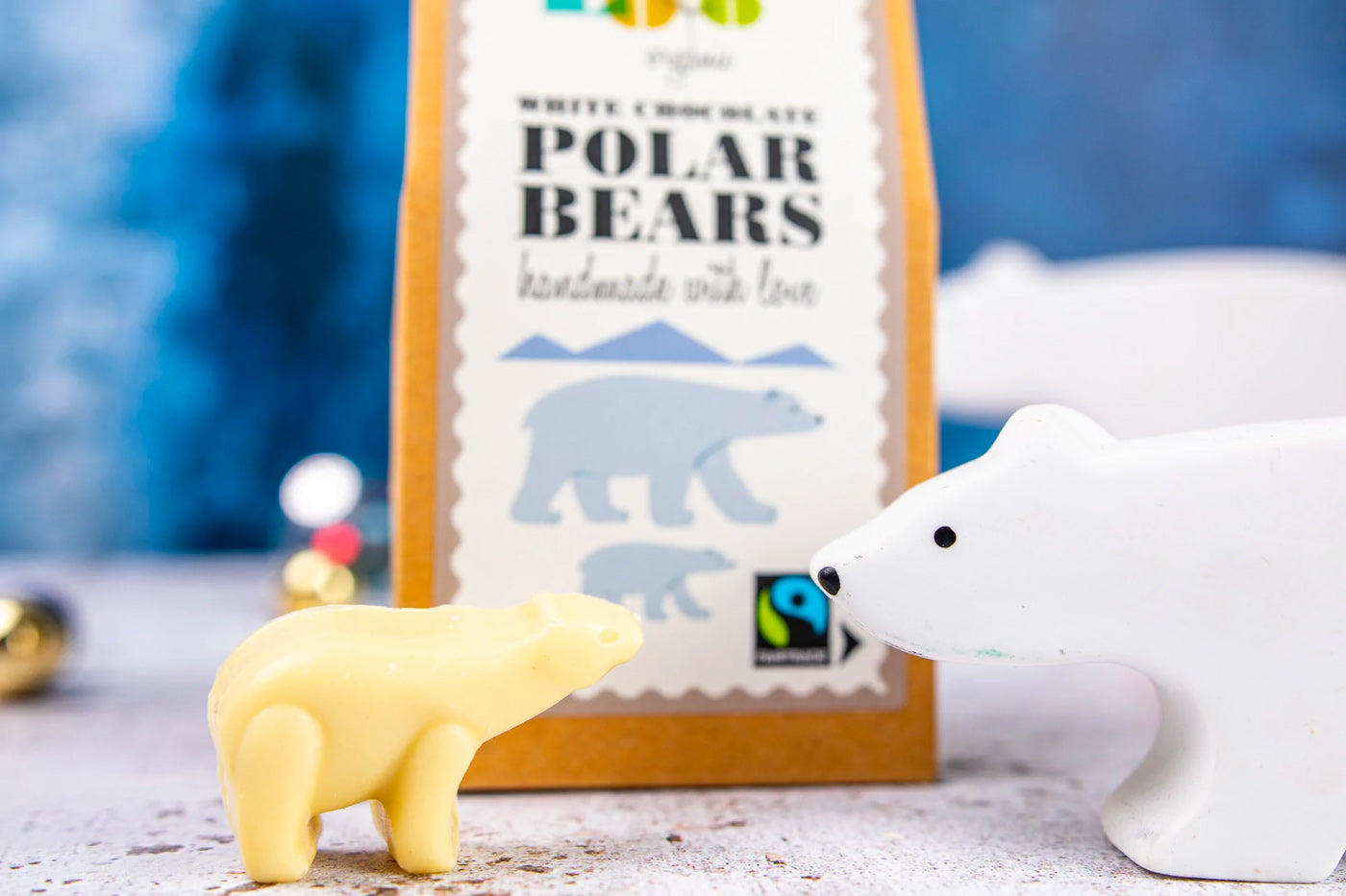 Close up of a Cocoa Loco white chocolate polar bear next to a wooden toy polar bear in front of its cardboard box