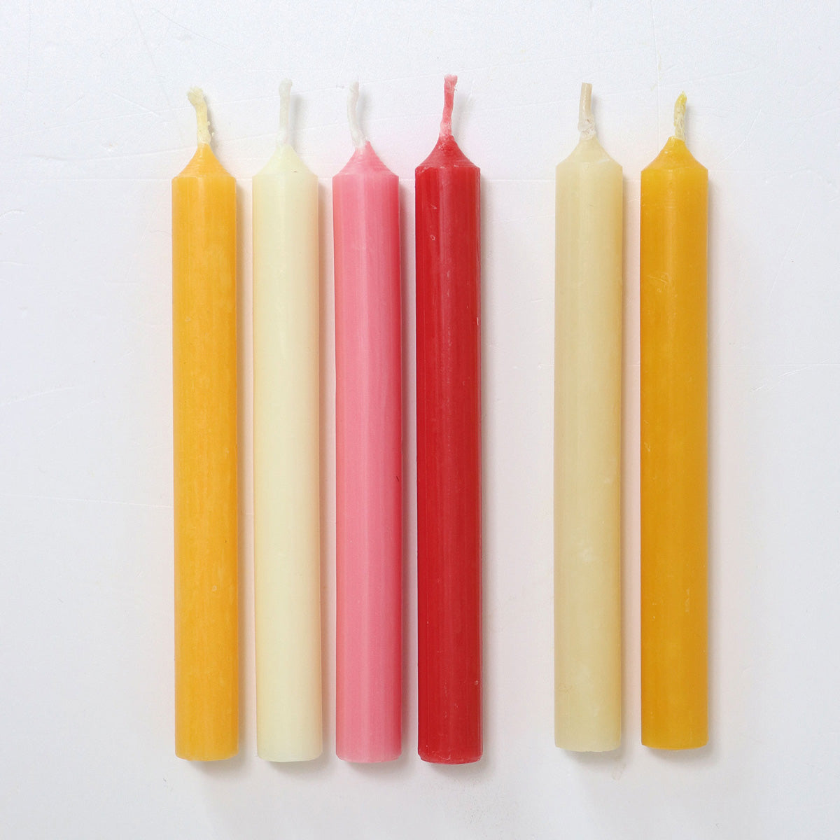 A pack of 12 Old Rose 10% beeswax candles by Grimm's with two pink candles outside the box. White background.