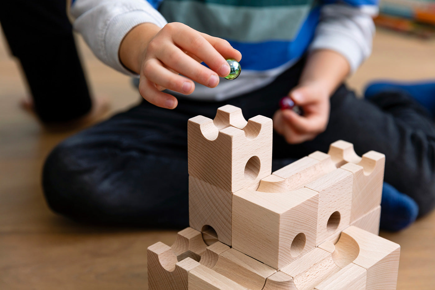 Close up of child holding a green glass marble above the Cuboro handmade wooden marble run building blocks