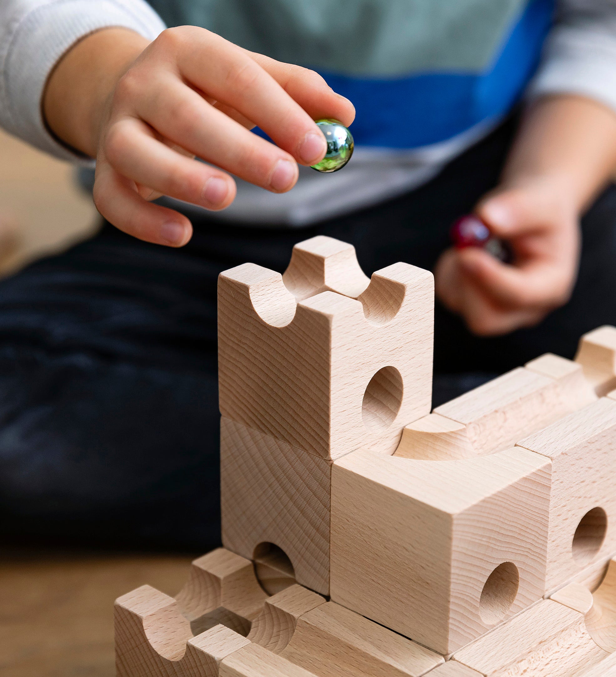 Close up of a child holding a green glass marble above a set of stacking Cuboro wooden marble run toy blocks