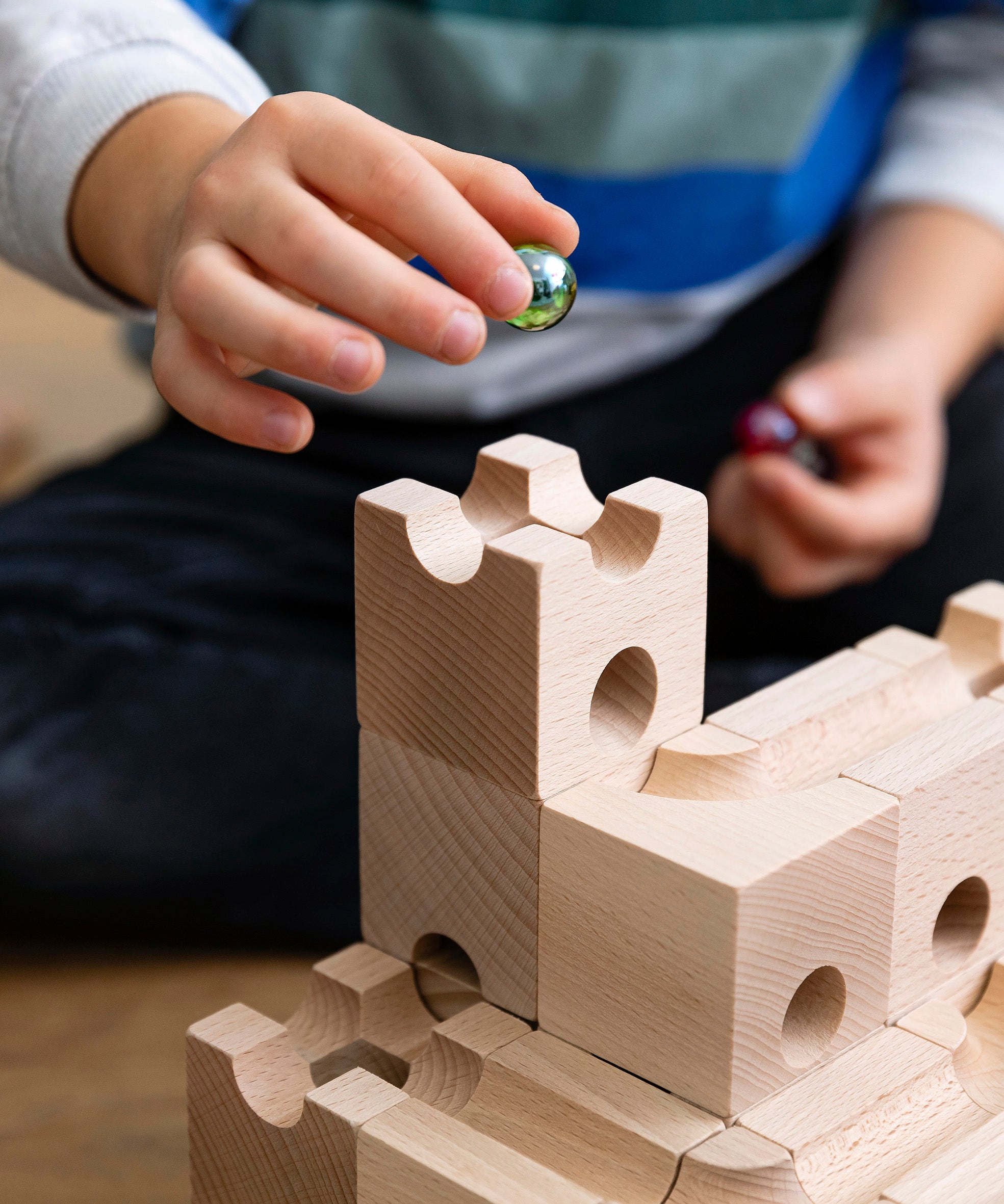 Close up of a child holding a green glass marble above a set of stacking Cuboro wooden marble run toy blocks