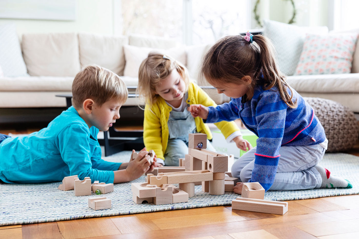 3 children playing with the Cuboro plastic-free wooden marble run toy set on a blue carpet