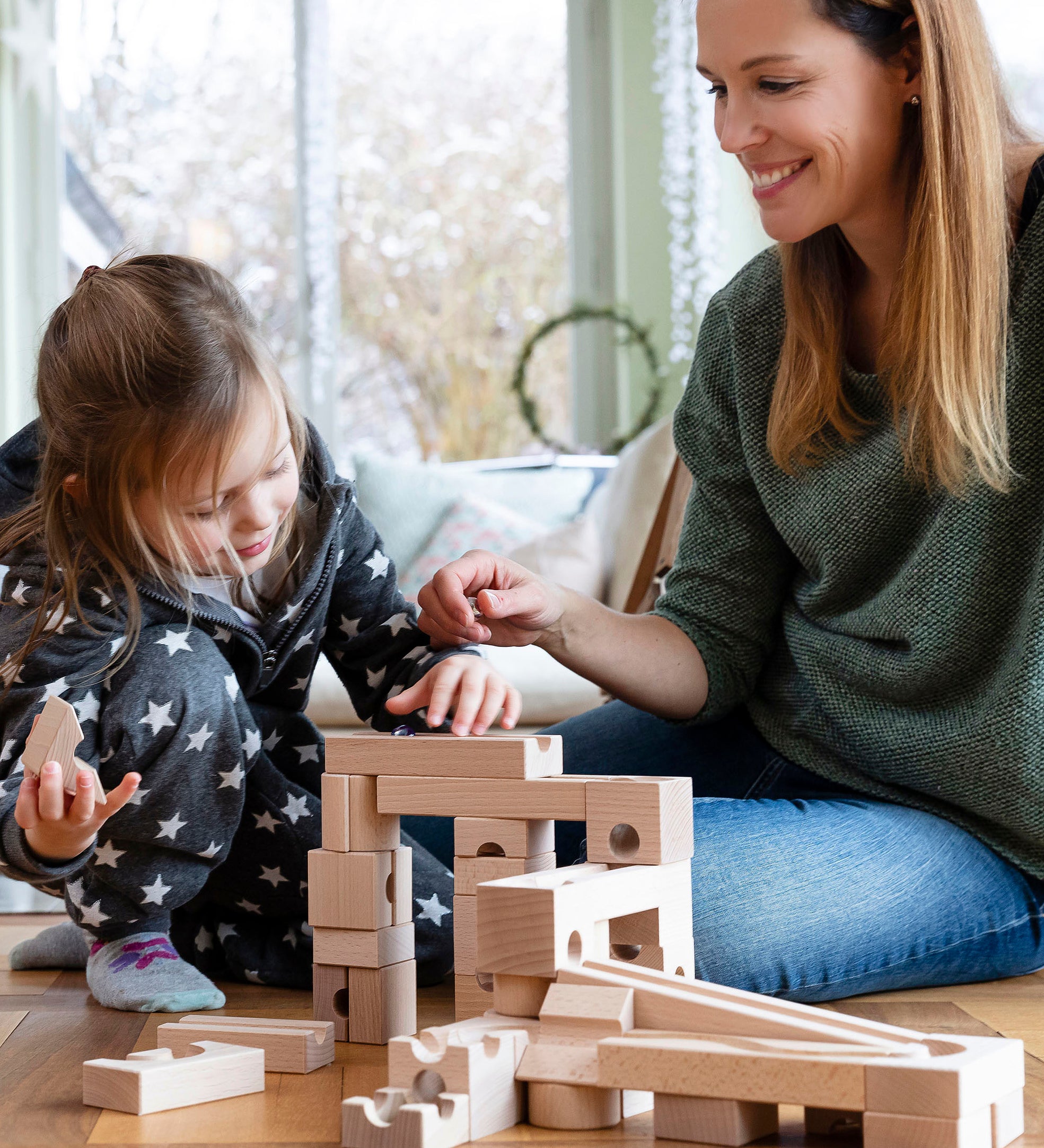 Child and adult sat on a wooden floor playing with the Cuboro handmade wooden marble run toy blocks