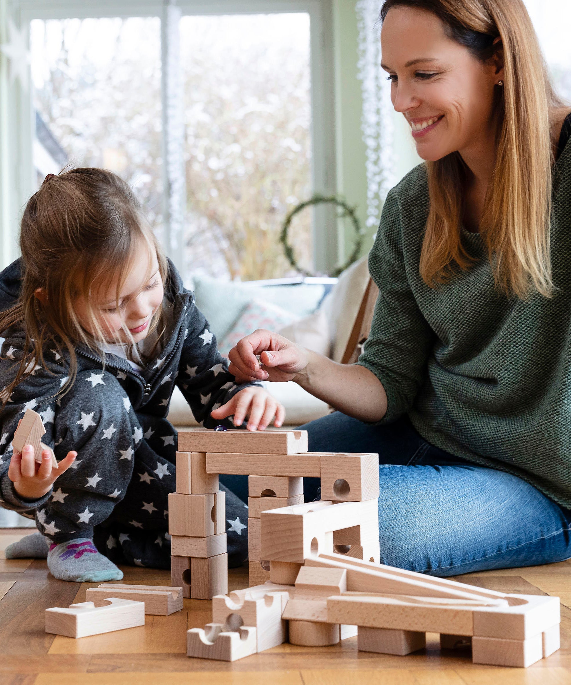 Child and adult sat on a wooden floor playing with the Cuboro handmade wooden marble run toy blocks