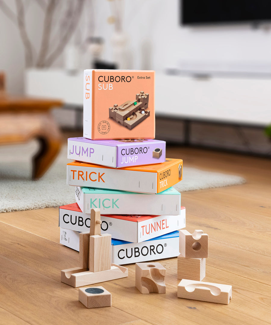 A stack of different Cuboro sets with pieces of the jump and kick sets on a wooden floor.