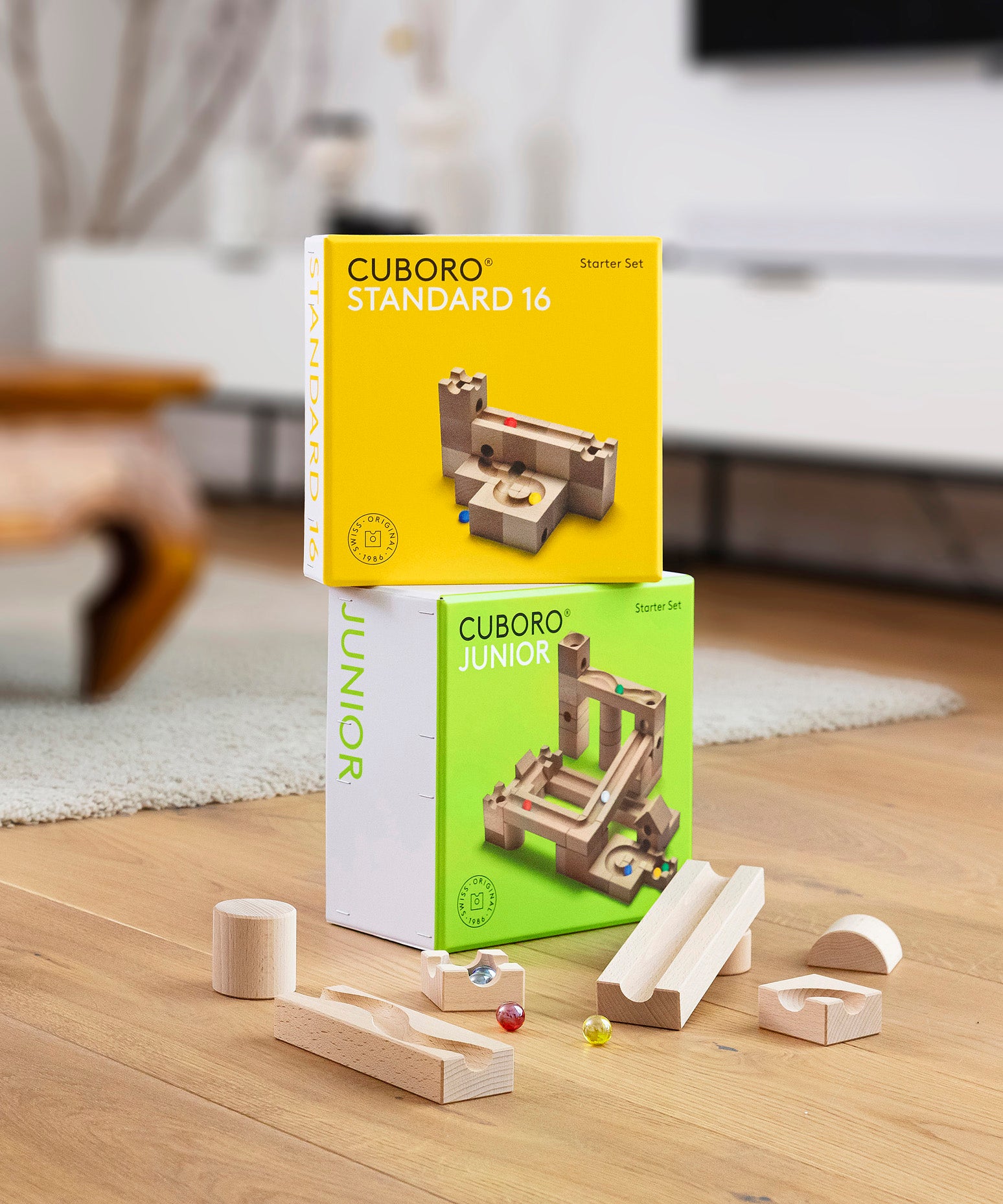 Boxes of the Cuboro Junior and Standard wooden marble run building kits on a wooden floor