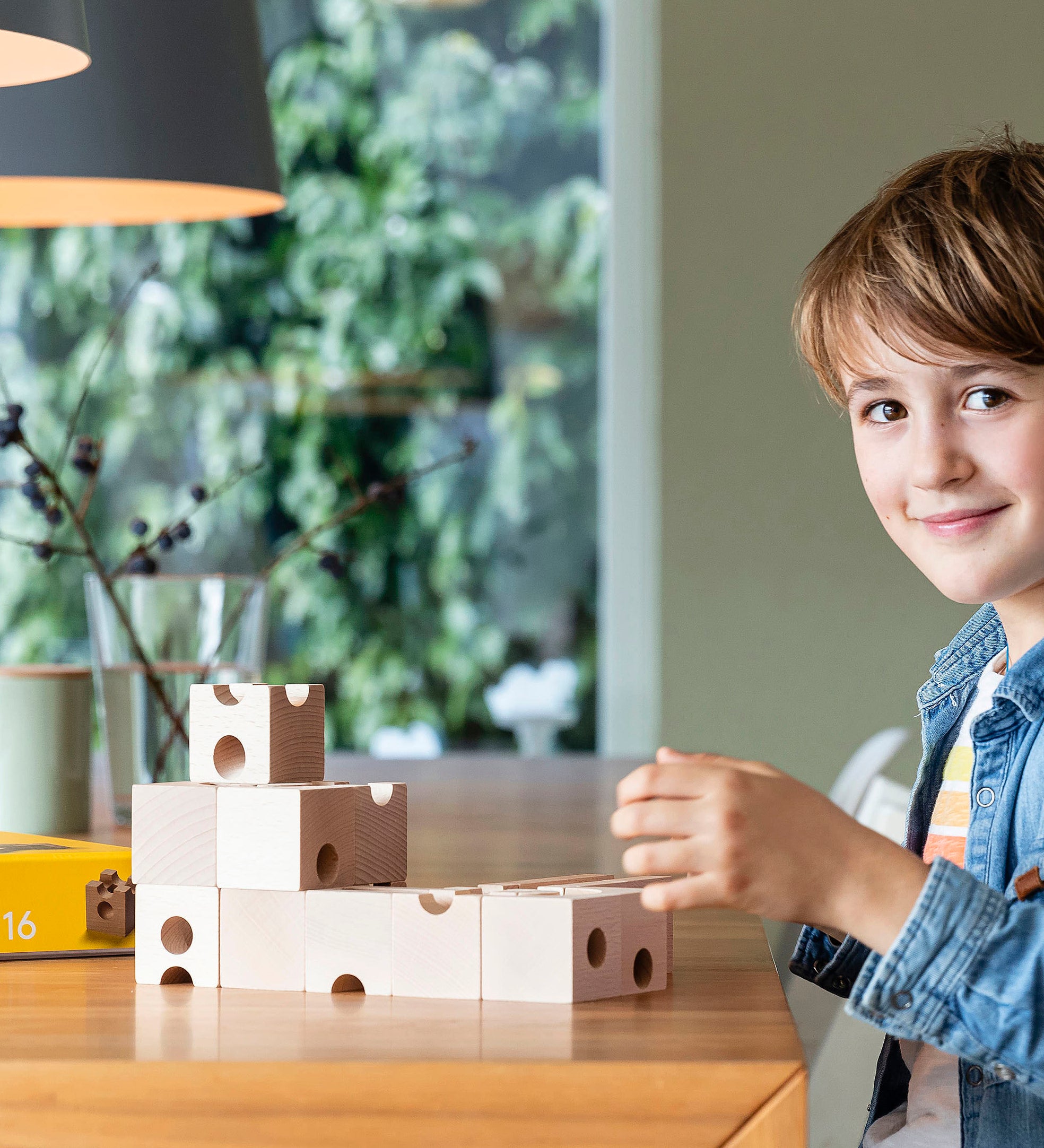 Young boy sat at a wooden table playing with the plastic-free Cuboro wooden marble run standard building kit