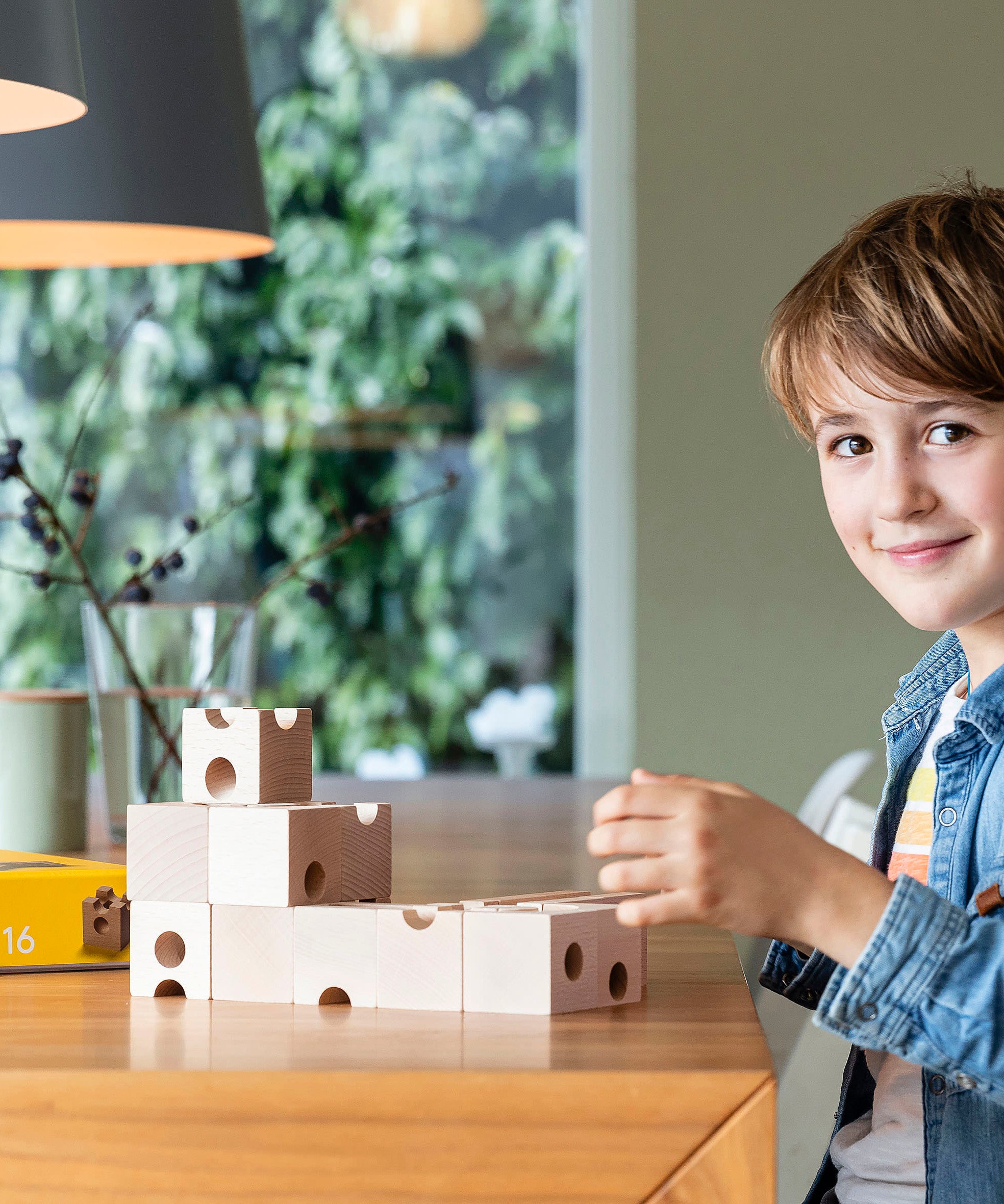 Young boy sat at a wooden table playing with the plastic-free Cuboro wooden marble run standard building kit