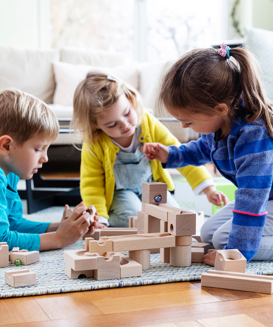 3 children playing with the Cuboro hand carved wooden marble run building blocks on a blue carpet