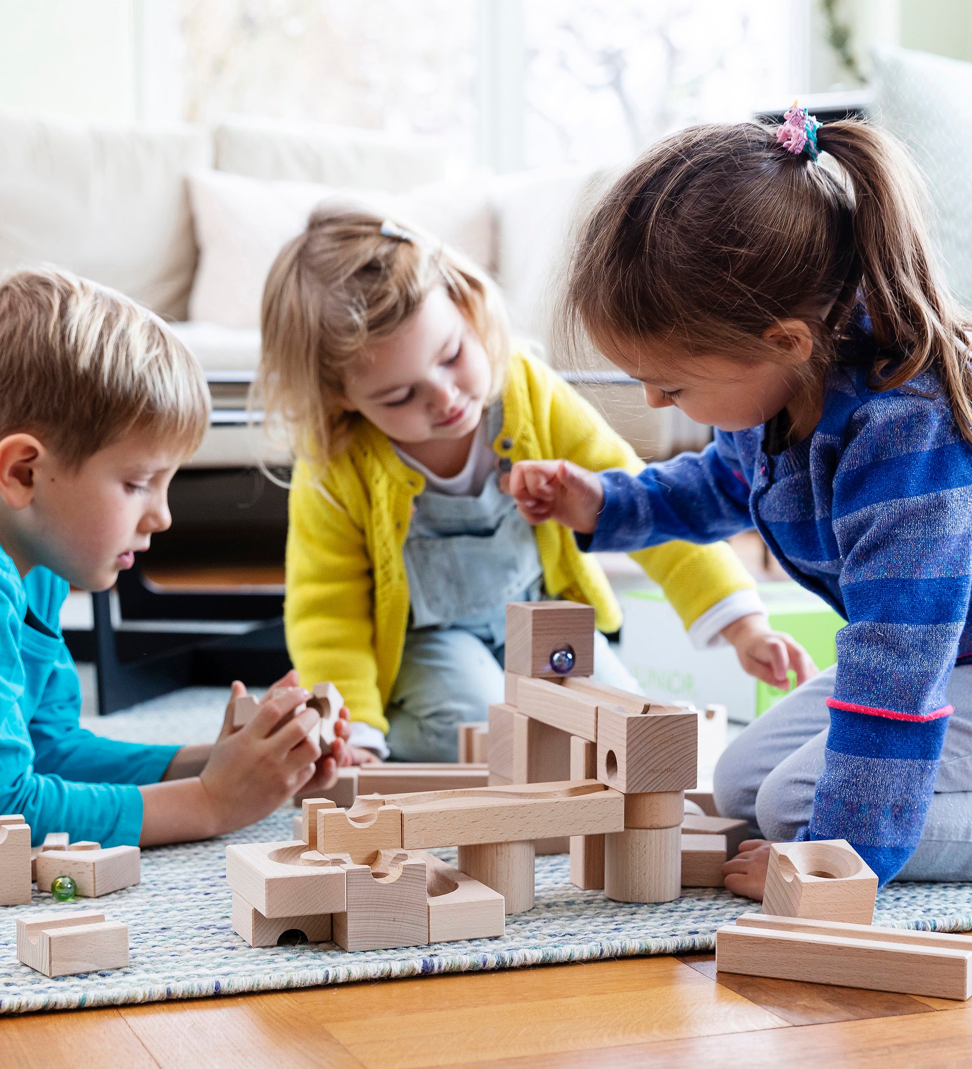 3 children playing with the Cuboro hand carved wooden marble run building blocks on a blue carpet