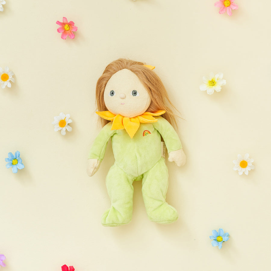 Olli Ella Dinky Dinkum Blossom Buds - Daisy  is sat in a flowerpot surrounded by the rest of the blossom bud range with a child holding Sunflower doll in the foreground