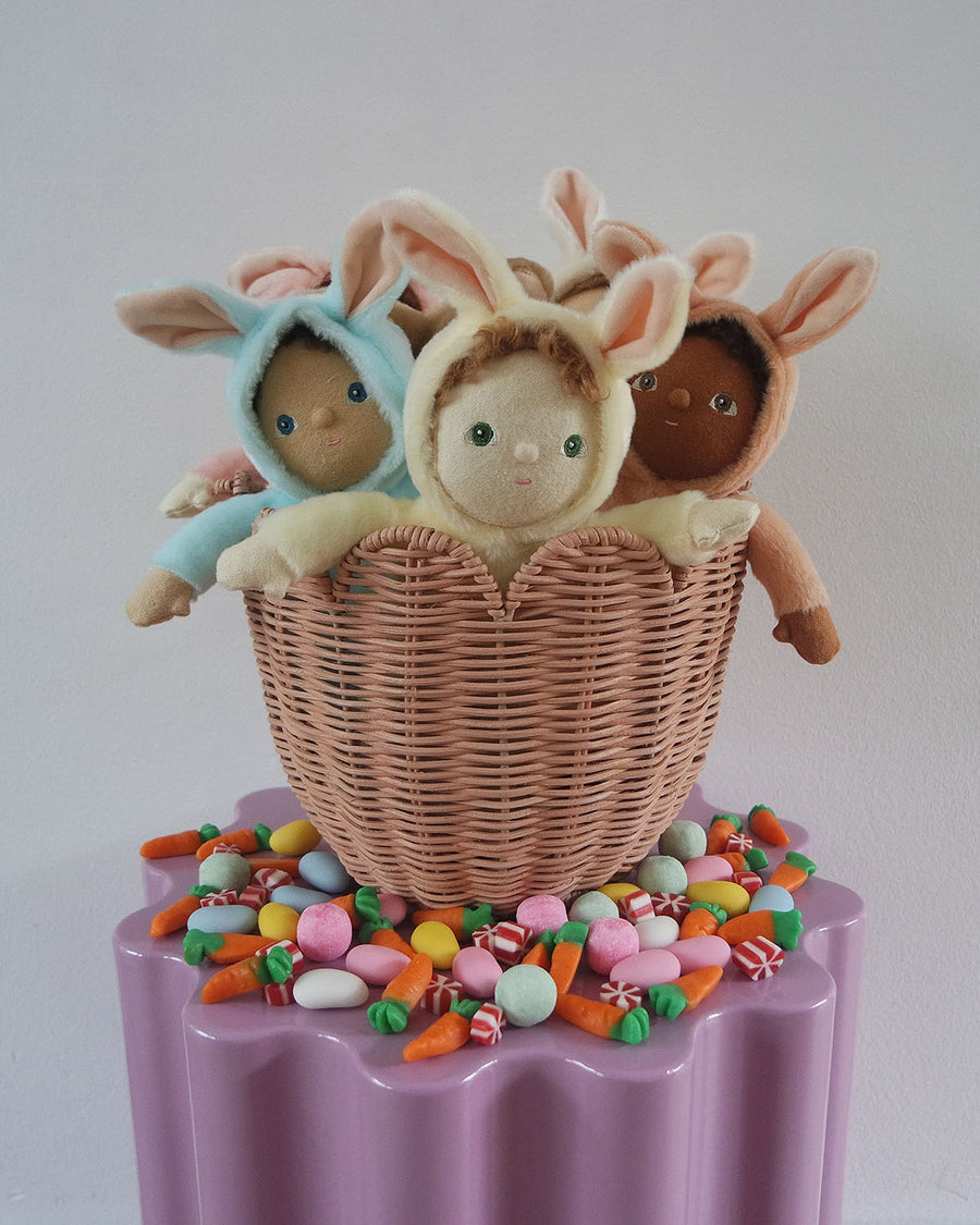 A pink Olli Ella Tulip basket holding the Olli Ella Dinky Dinkum Doll Fluffles collection on a table full of Easter sweets and decorations