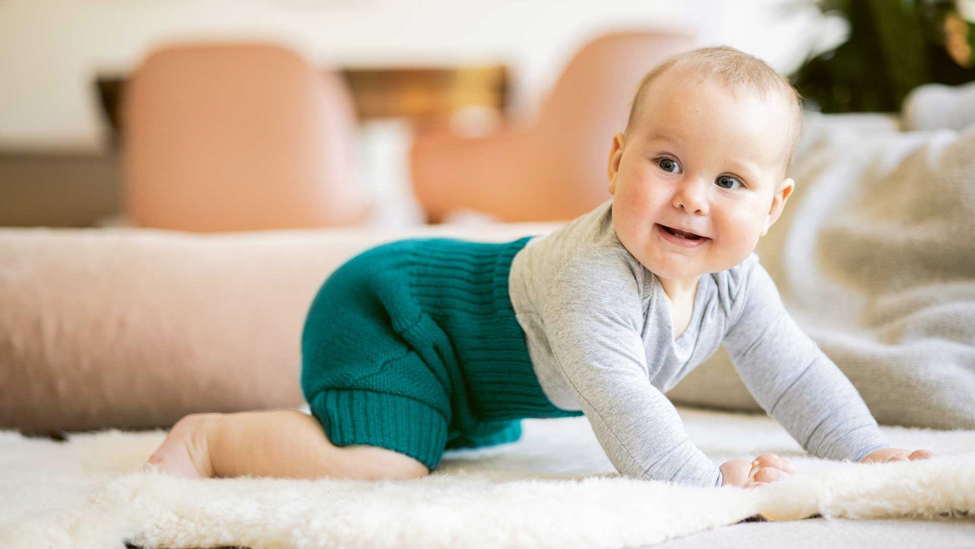 A little baby dressed in Disana cotton kids' clothing, crawling on the floor