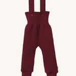 Disana organic merino wool dungarees in dark purple on a cream background.