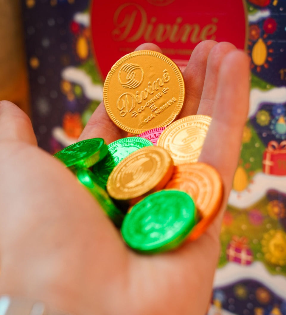 Close up of a hand holding the fairtrade Divine dark chocolate coins in front of a Divine christmas calendar