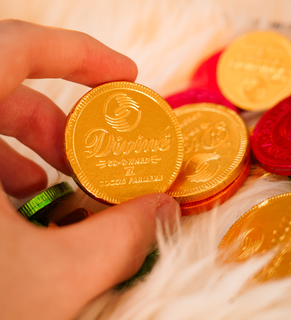 Close up of a hand holding a Divine ethical milk chocolate coin over a fluffy blanket