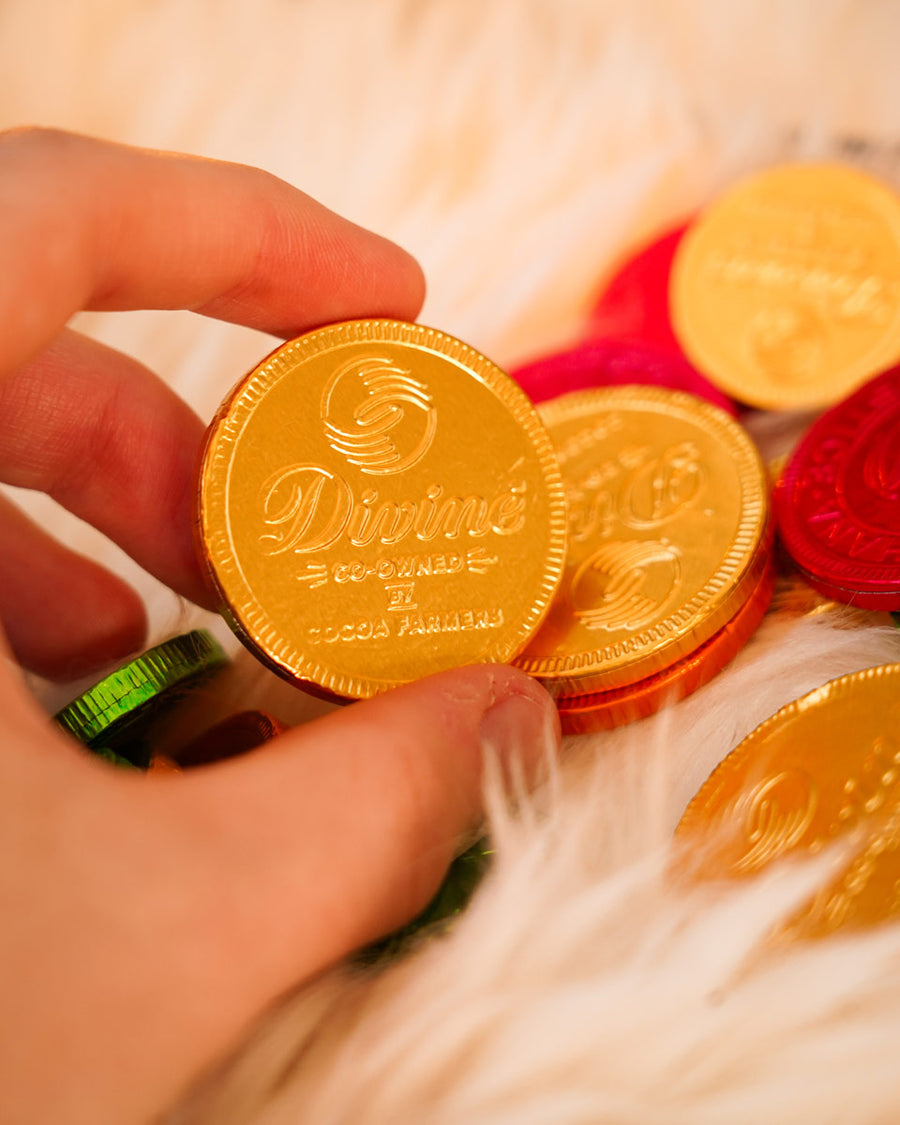 Close up of a hand holding a Divine ethical milk chocolate coin over a fluffy blanket