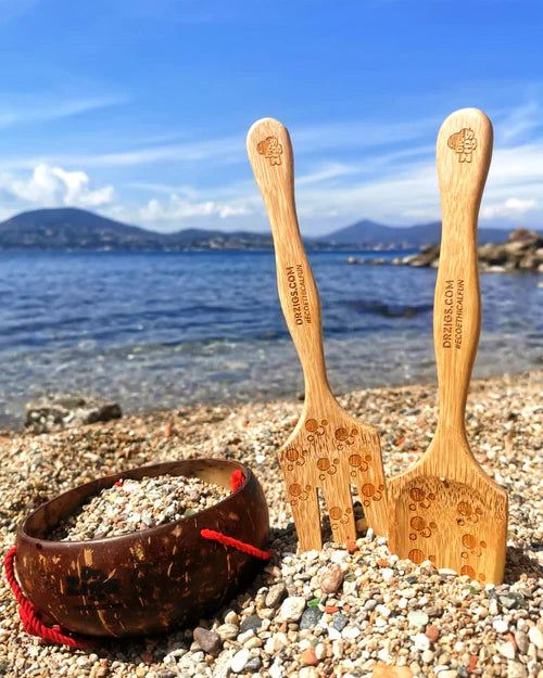 Dr Zigs Beach Creativity Kit shown on pebbles. The kit includes two bamboo tools and a coconut bowl. A mountain can be seen in the background