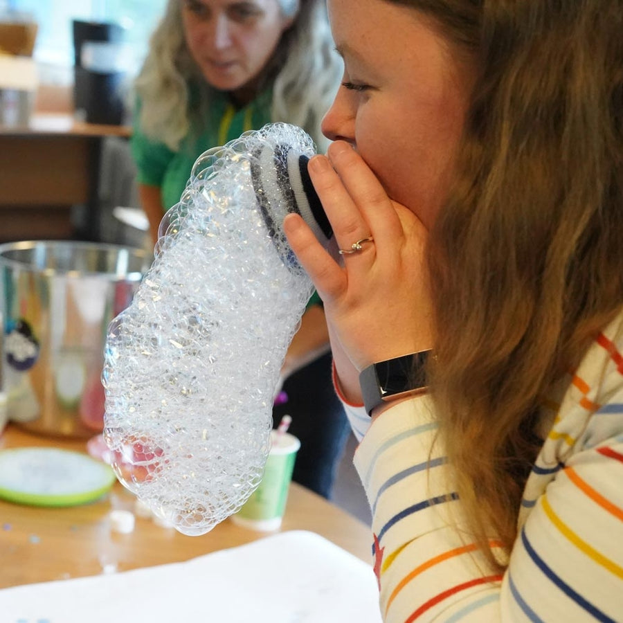 Close up of a child blowing bubbles with the Dr Zigs eco-friendly multi bubble wand on a pebble beach