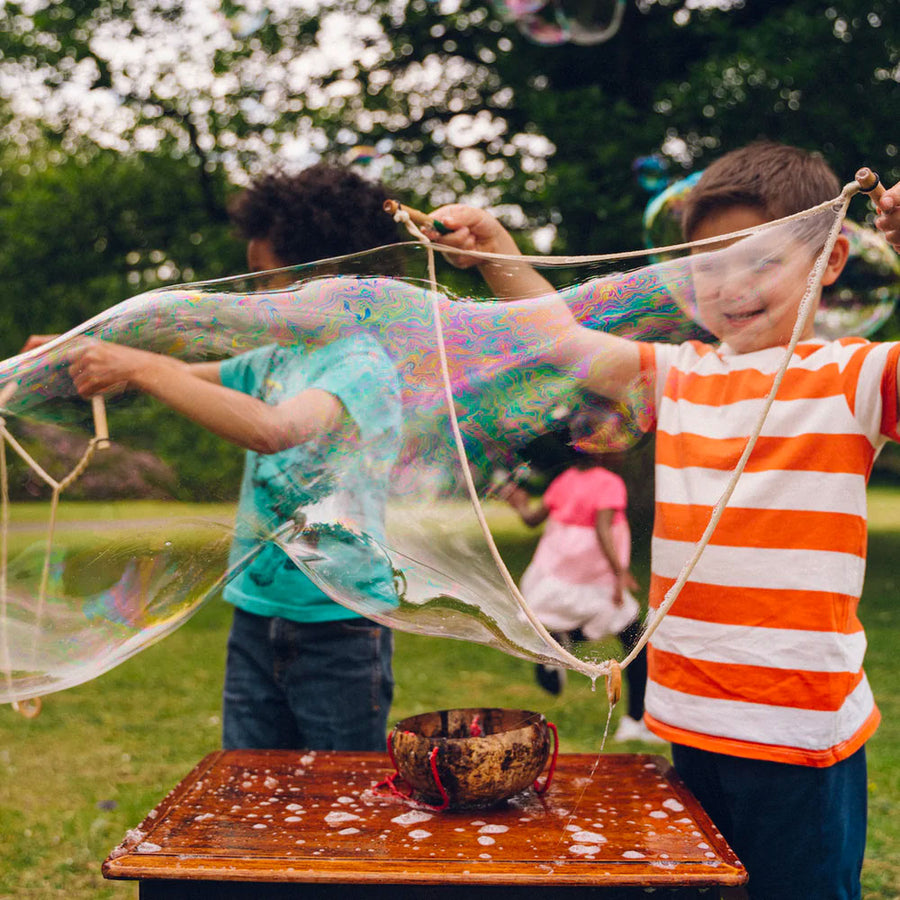 2 children blowing bubbles with the Dr Zigs giant bubble wand above the Dr Zigs coconut bucket