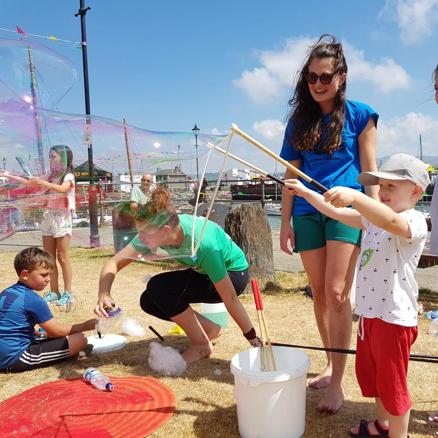 Child stood holding up the Dr Zigs giant bubble wand over a white bucket with a large bubble floating out