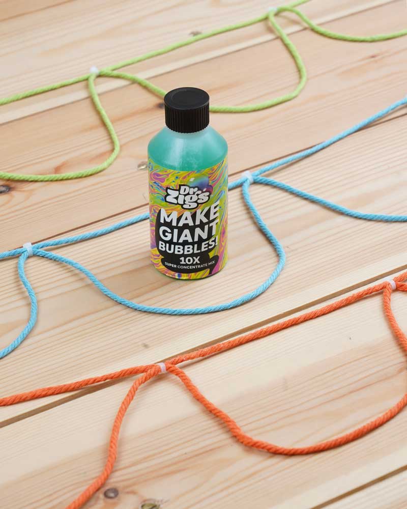 Close up of the Dr Zigs 10x concentrated bubble mixture on a wooden floor next to some coloured rope bubble blowers