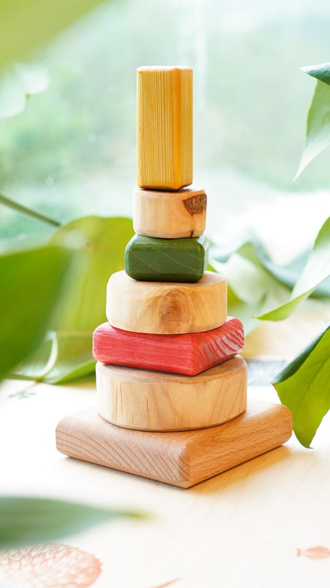 Drei Blatter eco-friendly wooden stacking puzzle on a wooden background between some large leaves