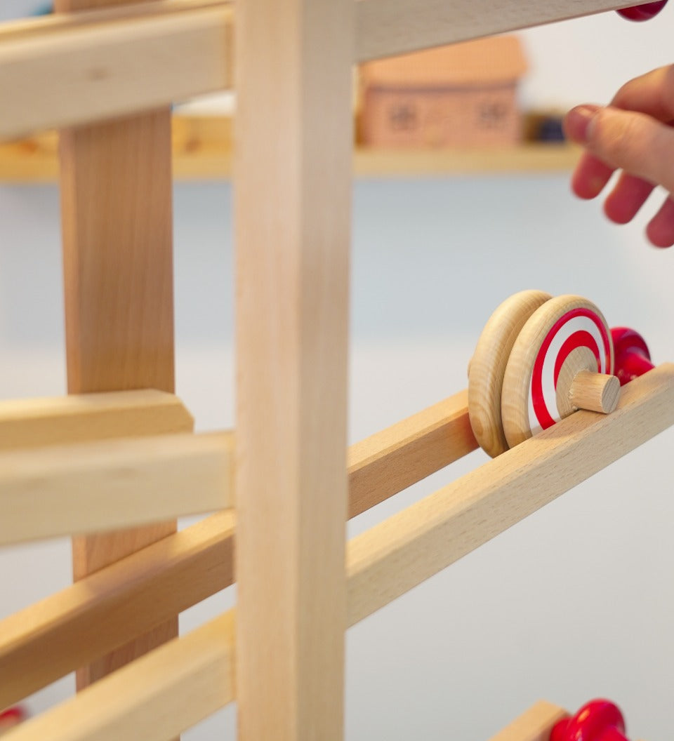 Close up of a hand rolling the Fagus wooden spiral disc toy down a Fagus wooden marble run set