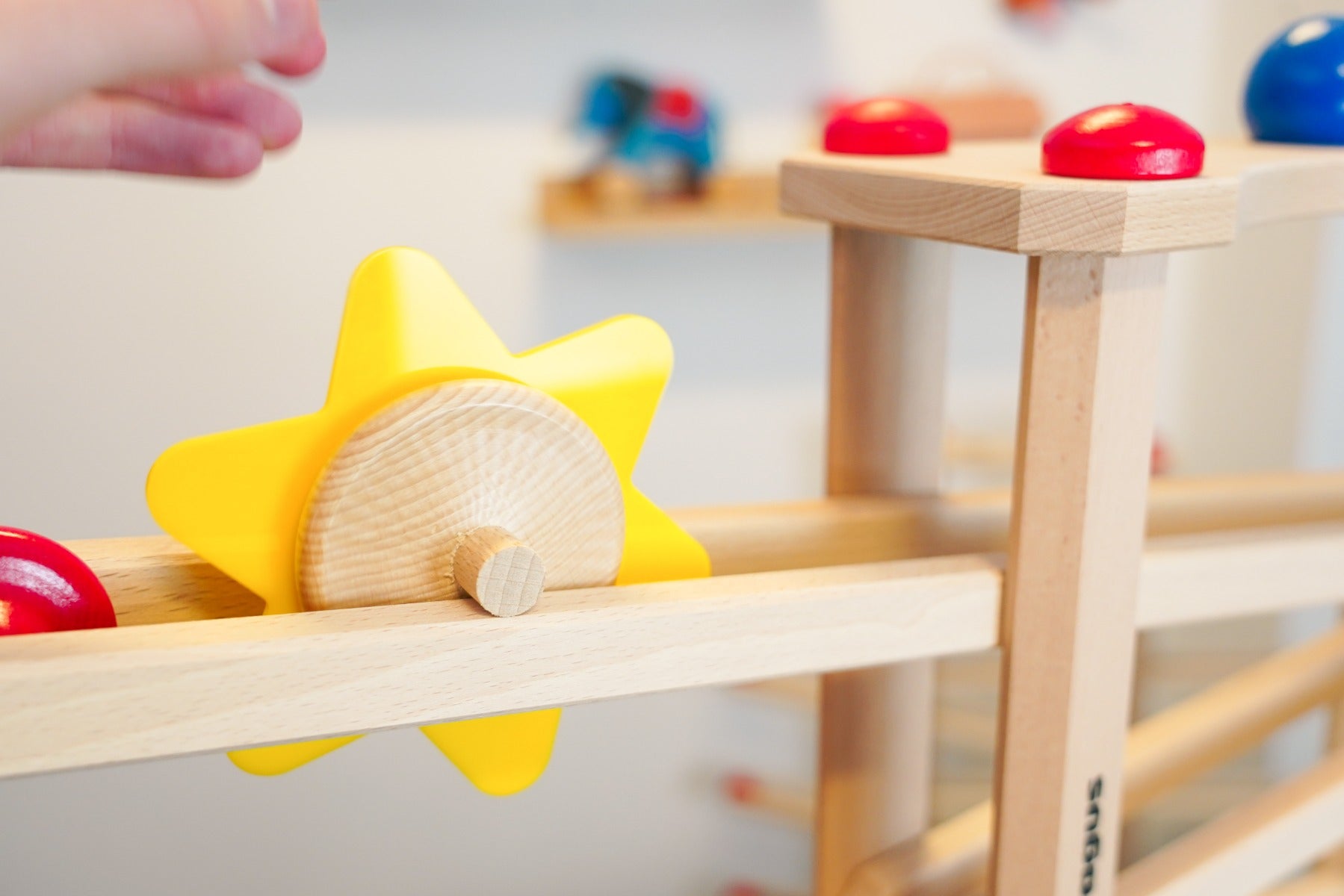 Close up of a hand rolling the Fagus spinning sun toy down a Fagus wooden marble run