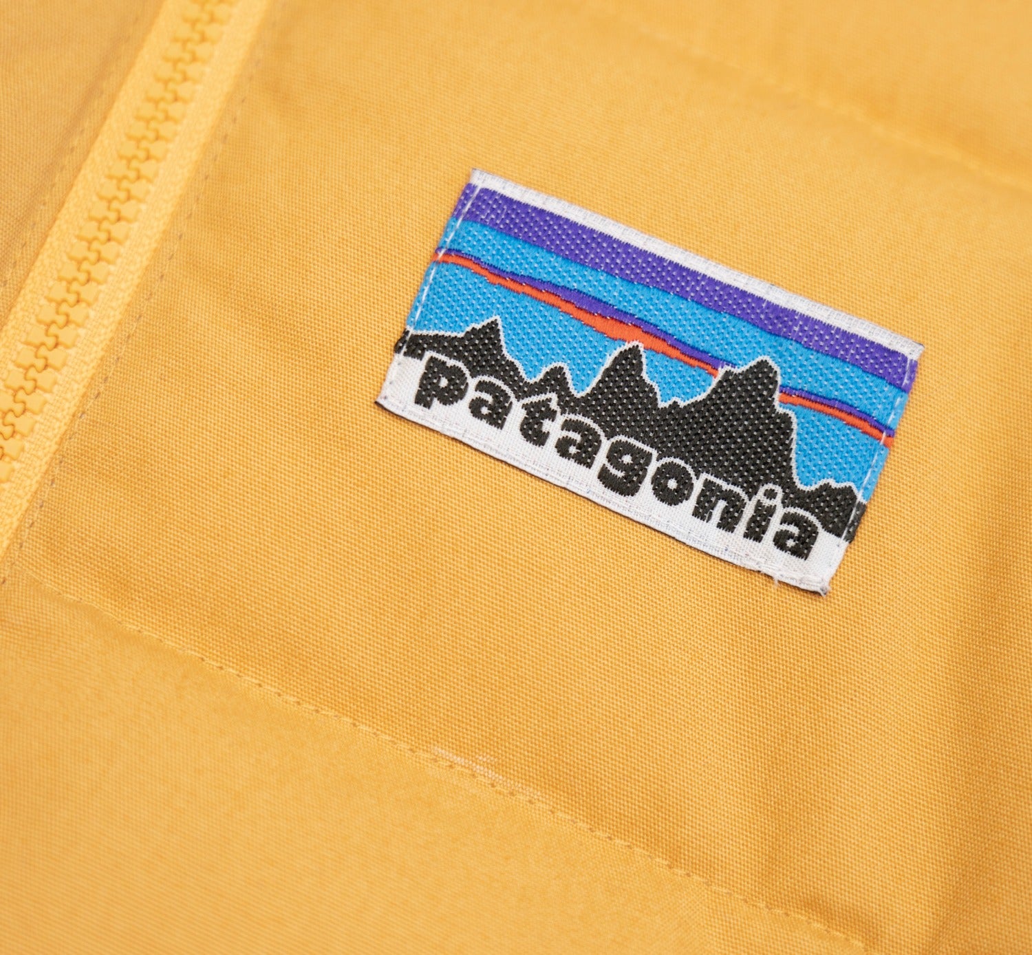 Patagonia Kids Cotton Quilted Down Jacket - Dried Mango. Logo detail close-up.