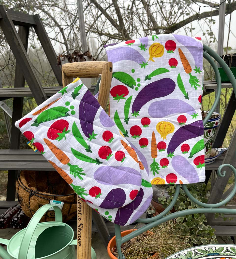 DUNS Sweden organic cotton linen oven glove and tea towel in the cultivate print hanging over the end of a metal chair