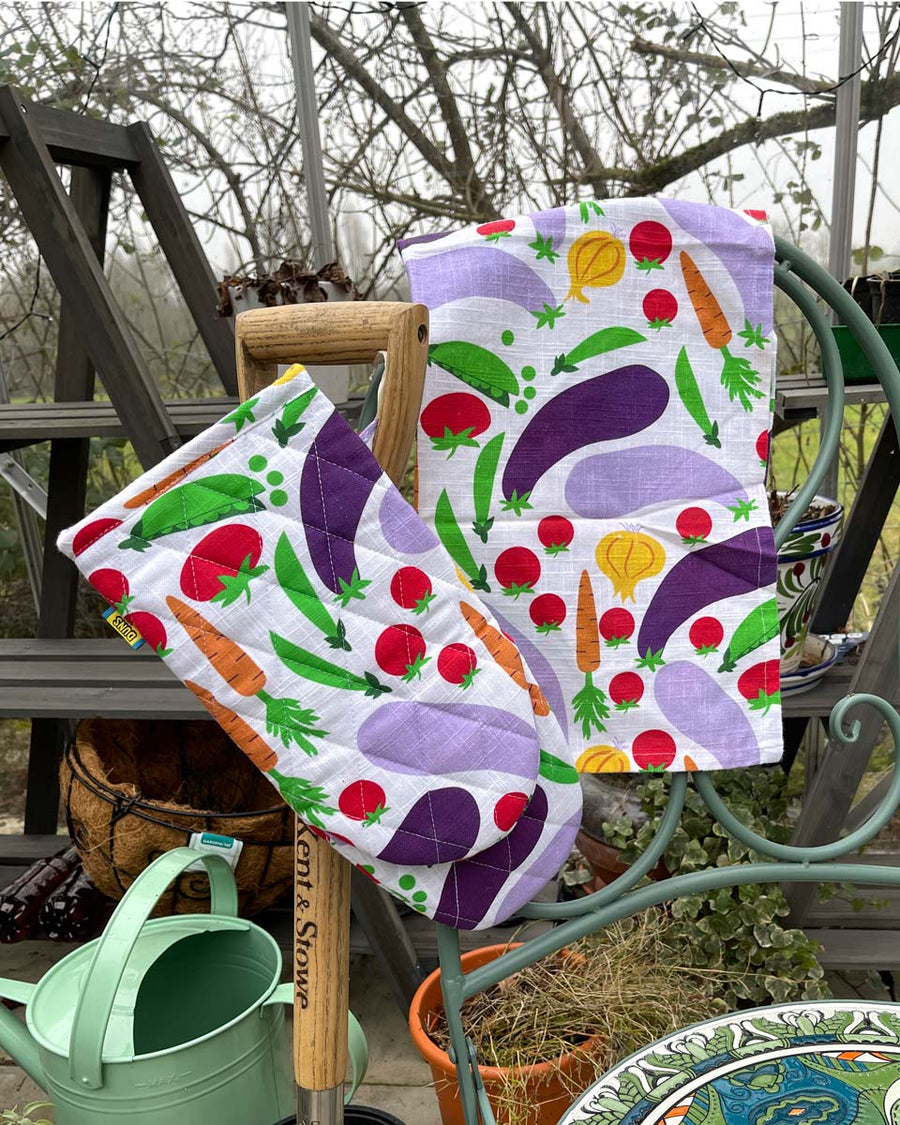 DUNS Sweden organic cotton linen oven glove and tea towel in the cultivate print hanging over the end of a metal chair