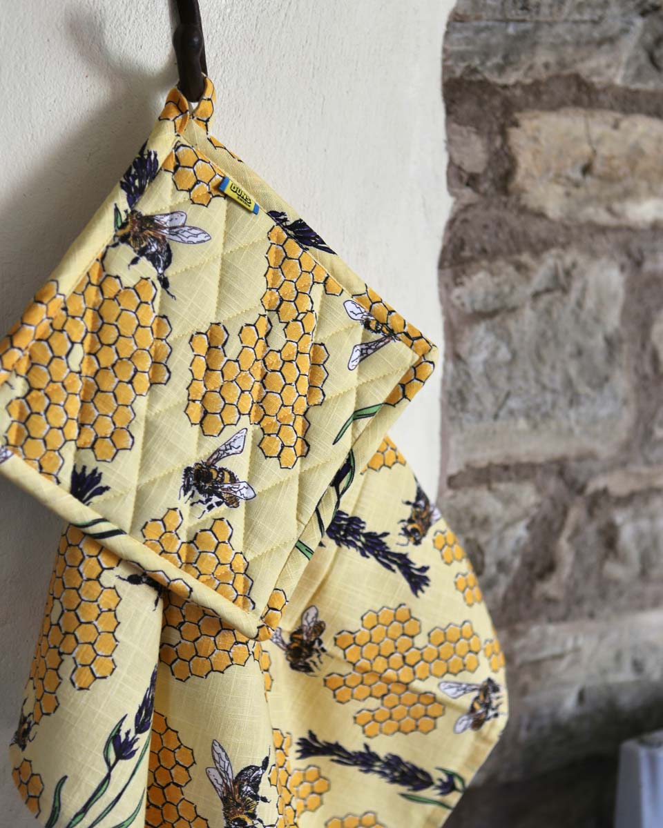 DUNS Sweden organic cotton linen pot holder and tea towel in the bee yellow print handing from a metal hook next to a stone wall