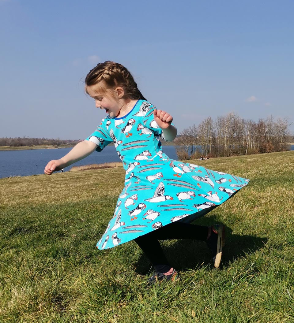 Girl running on some grass wearing the DUNS Sweden organic cotton skater dress in the blue puffin print