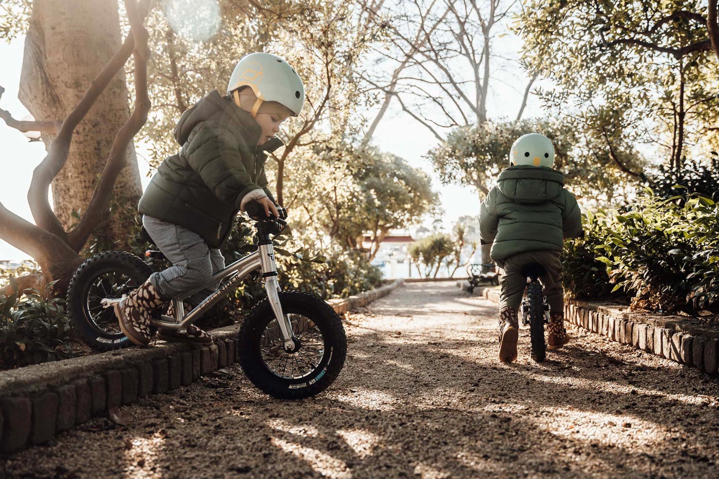 2 children sat on Early Rider aluminium balance bikes on a rock in front of the sea