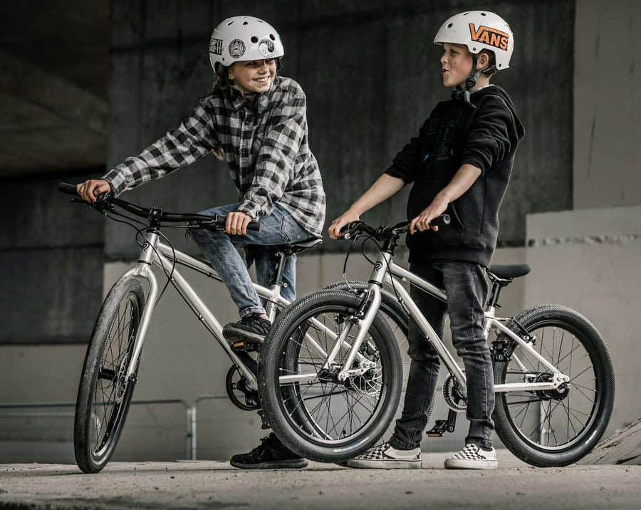 Two children getting ready to cycle on the Early Rider kids Belter 20" Bike in Brushed Aluminum