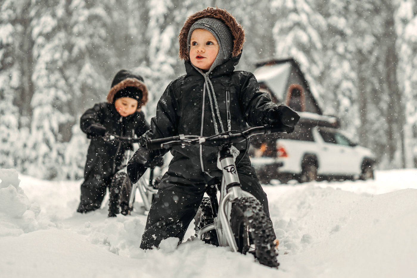 2 kids sat on some Early Rider 12 inch balance bikes in some deep snow