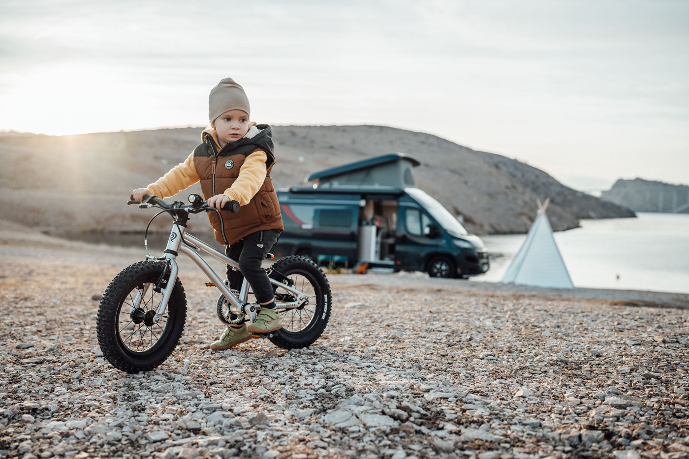 Girl sat on an Early Rider 14 inch seeker bicycle in front of a black campervan