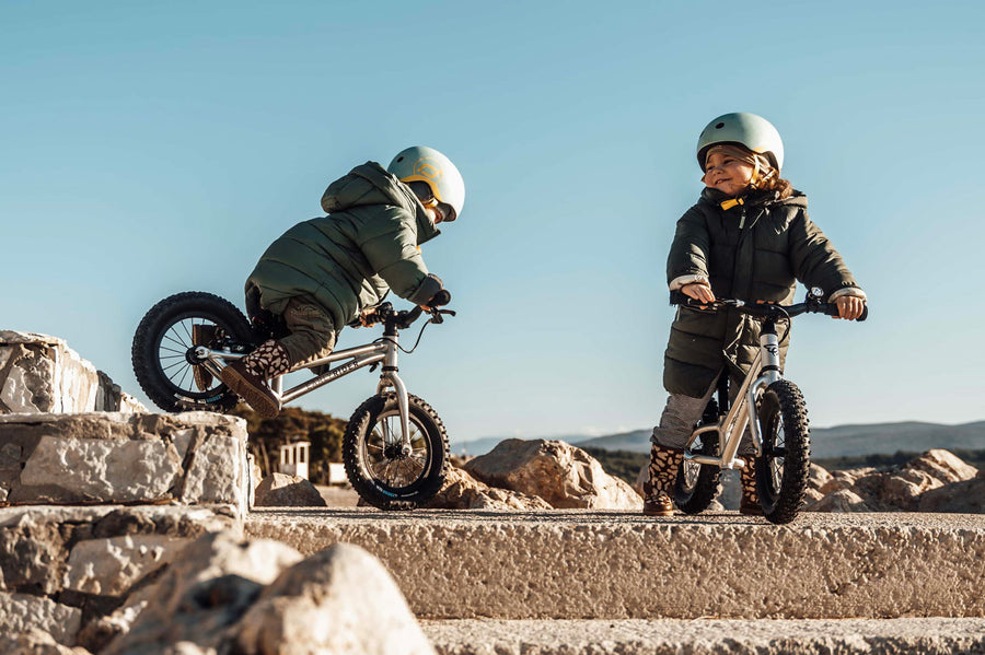 2 children riding Early Rider big foot balance bikes down a gravel path