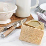 Eco Living plastic free kitchen and bathroom loofah scrub pad on a white worktop in front of some white kitchen utensils