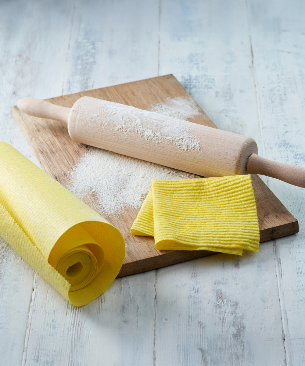 Ecoliving yellow compostable sponge kitchen roll next to a wooden board and rolling pin